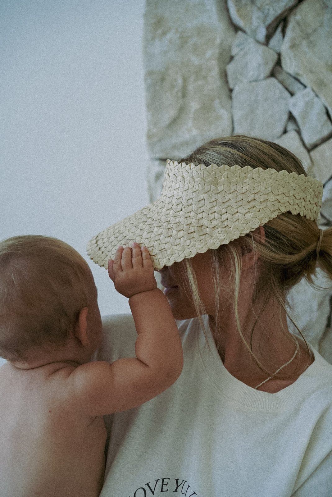 Baby playing with mother's woven visor hat outdoors