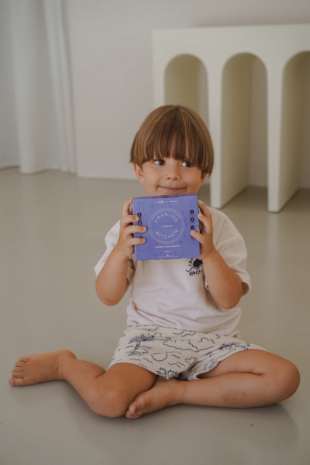 Young boy sitting cross-legged holding a box of Franjo's Kitchen kids' biscuits