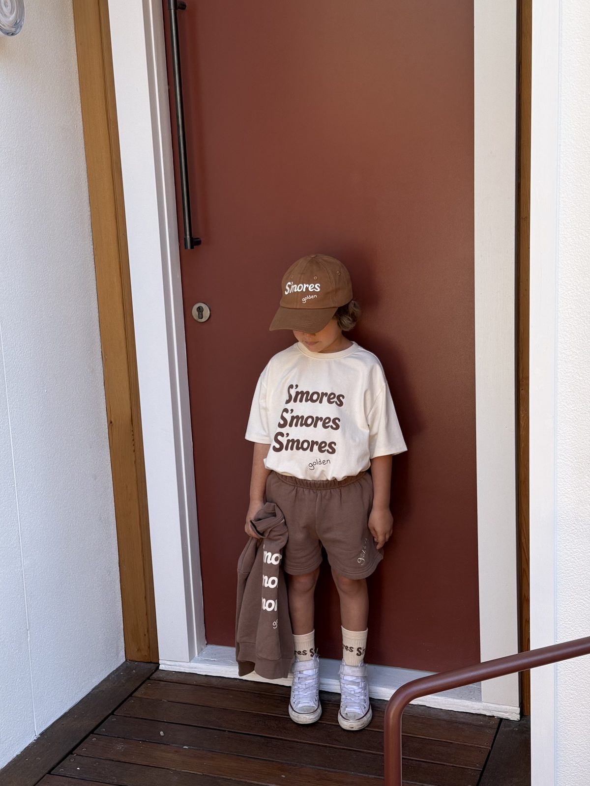 Boy in brown S'mores-print cap and tee standing in a doorway