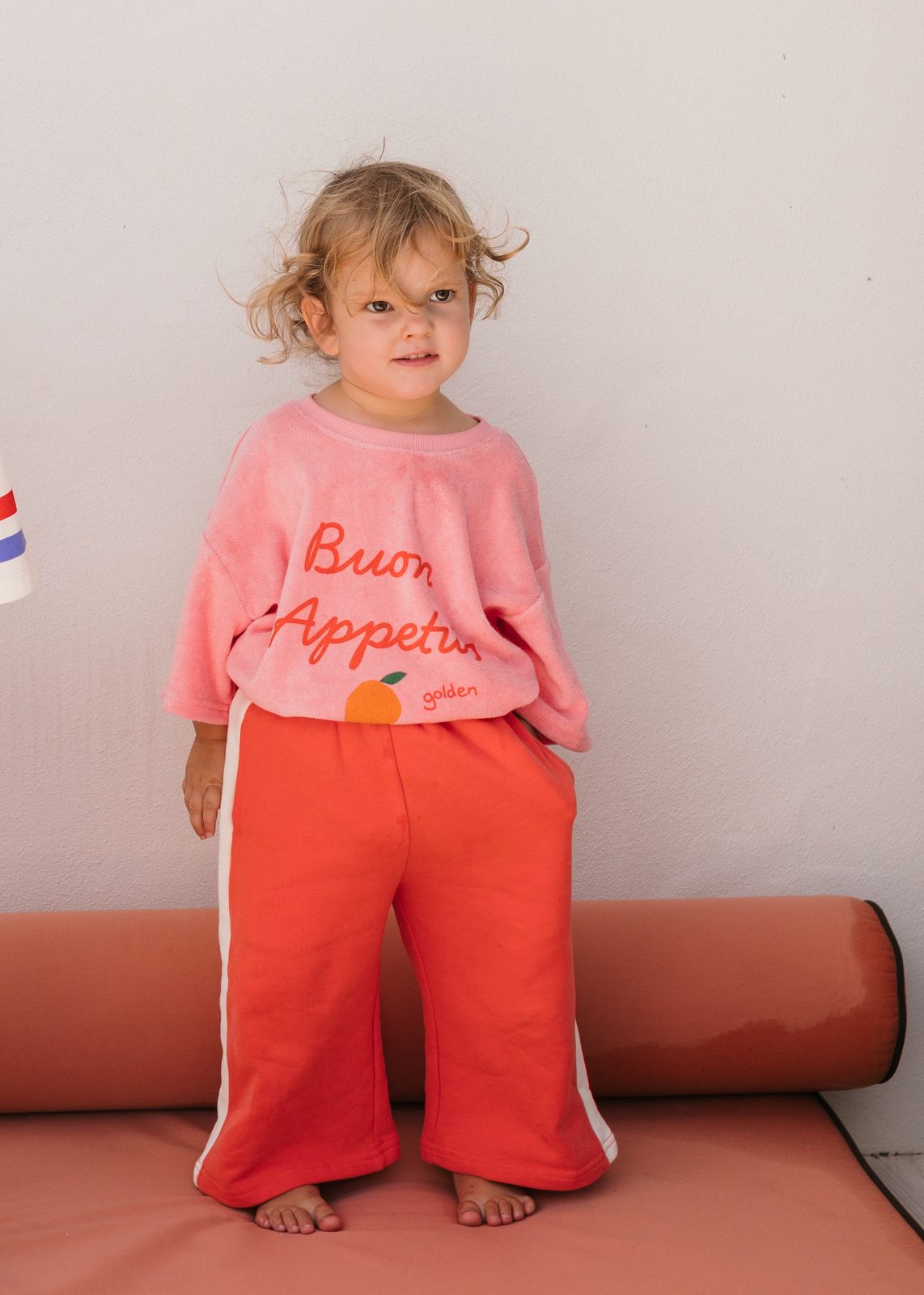 Toddler girl in a pink 'Buon Appetito' top and orange trousers for a Golden clothing campaign