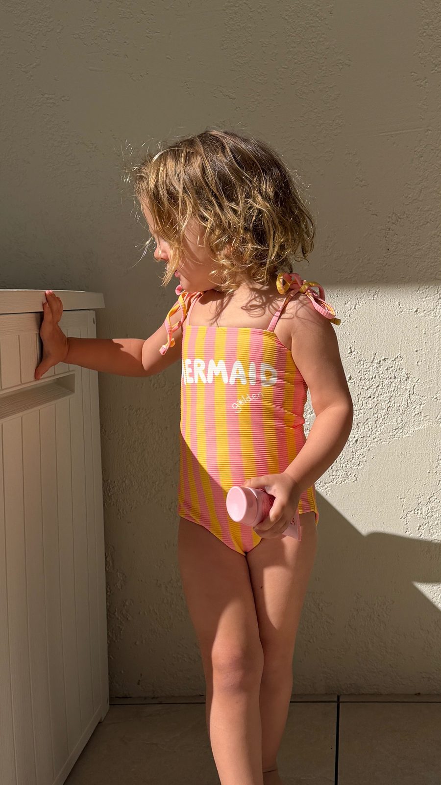 Girl in pink and yellow striped 'Mermaid' one-piece swimsuit in sunlight