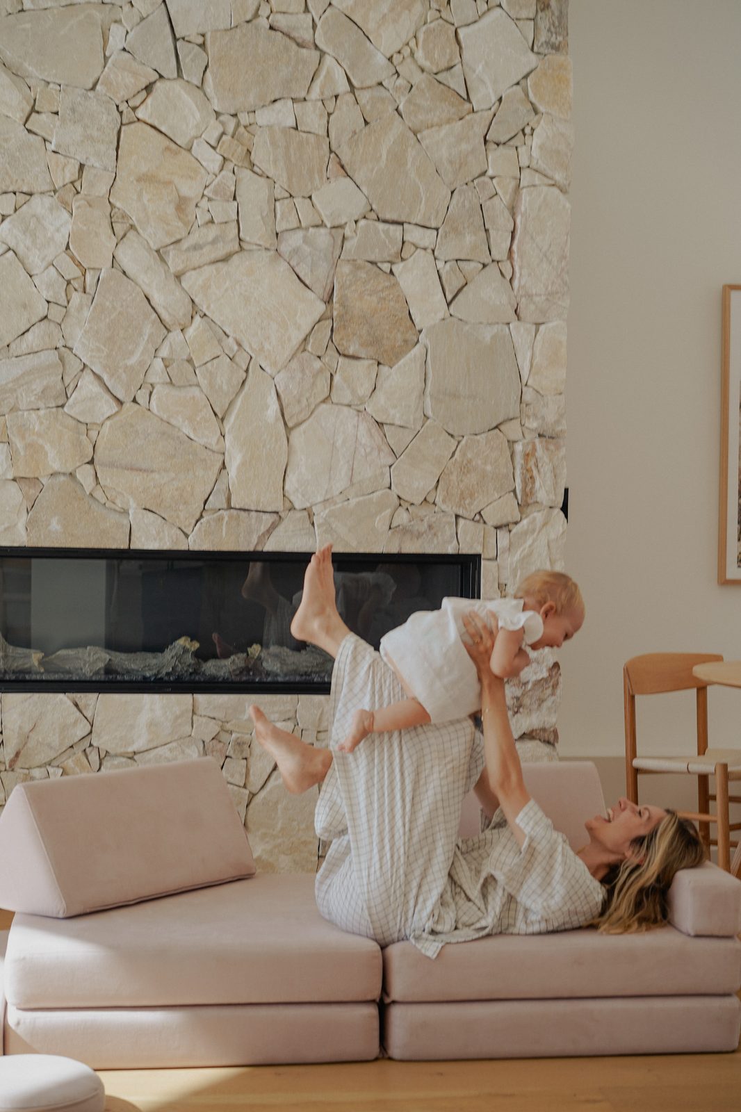 Mother lifting giggling baby overhead on a couch by the fireplace