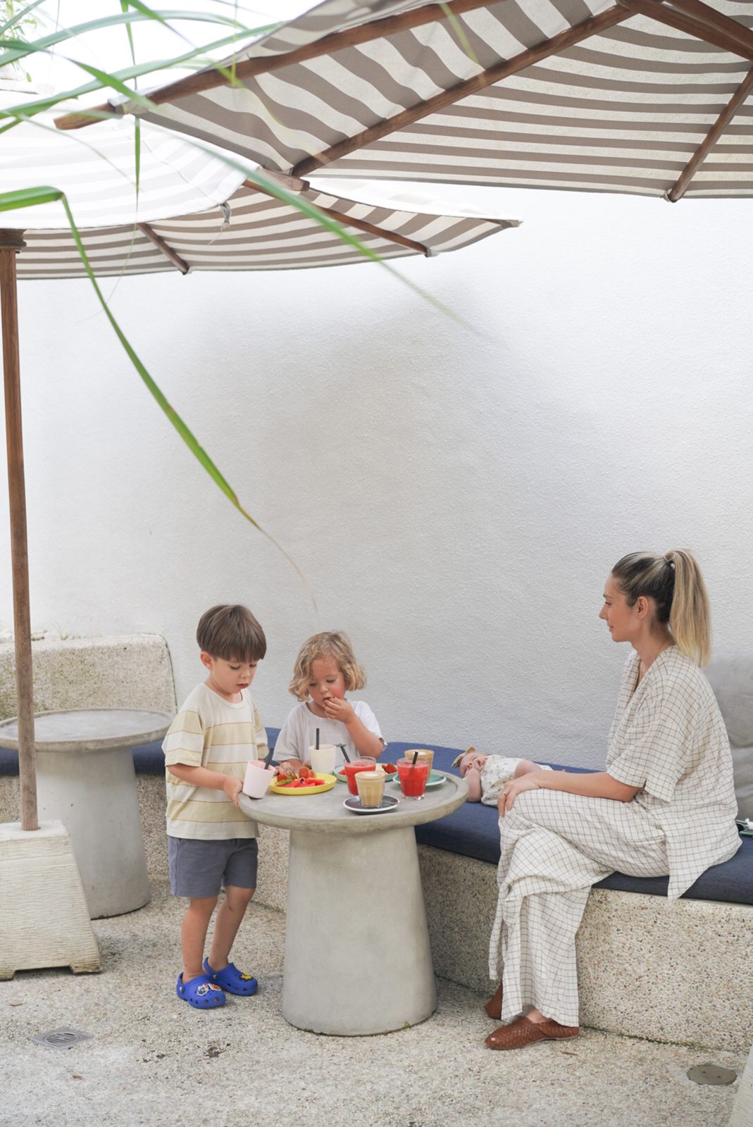 Two young children sharing a snack at an outdoor cafe table with their mother
