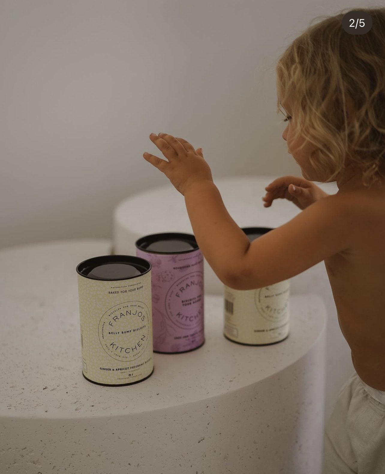 Toddler reaching toward a display of Franjos Kitchen pregnancy biscuit tins