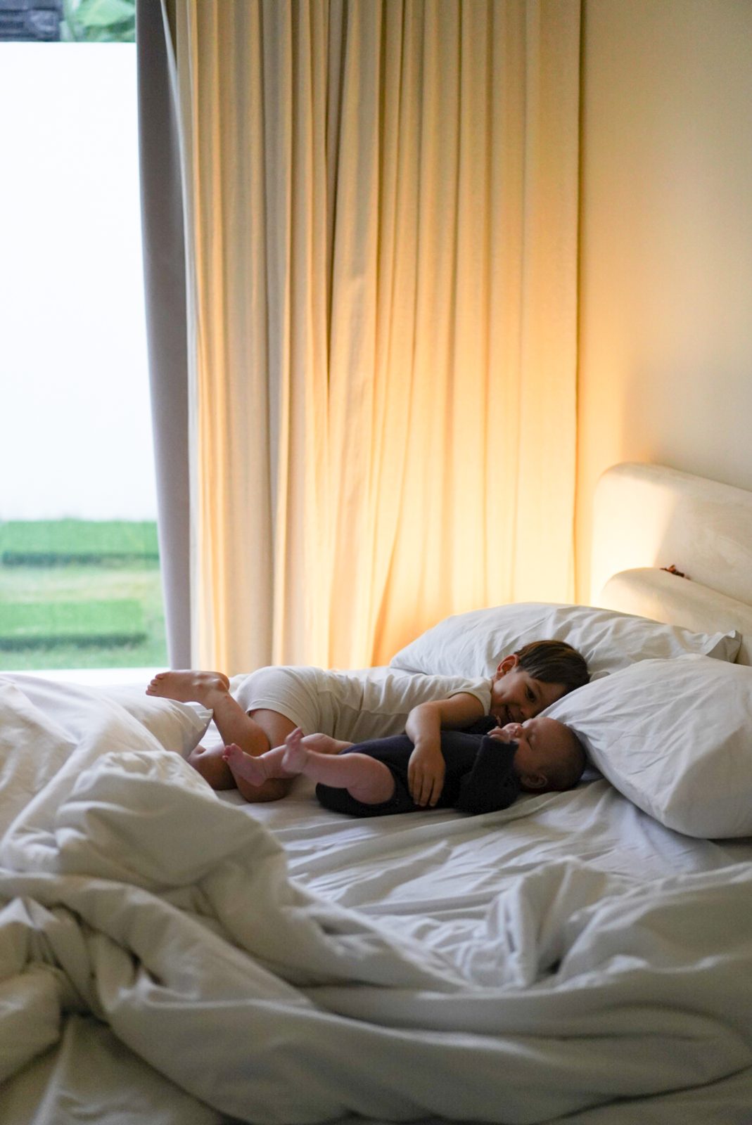 Older sibling lying on a bed smiling at a newborn baby