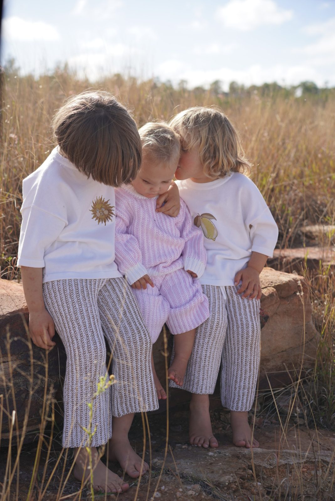 Two young siblings in knit sweaters embracing outdoors at golden hour