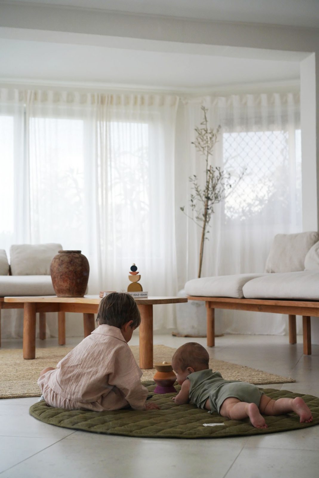 Older sibling and baby playing together with a wooden toy on a round rug