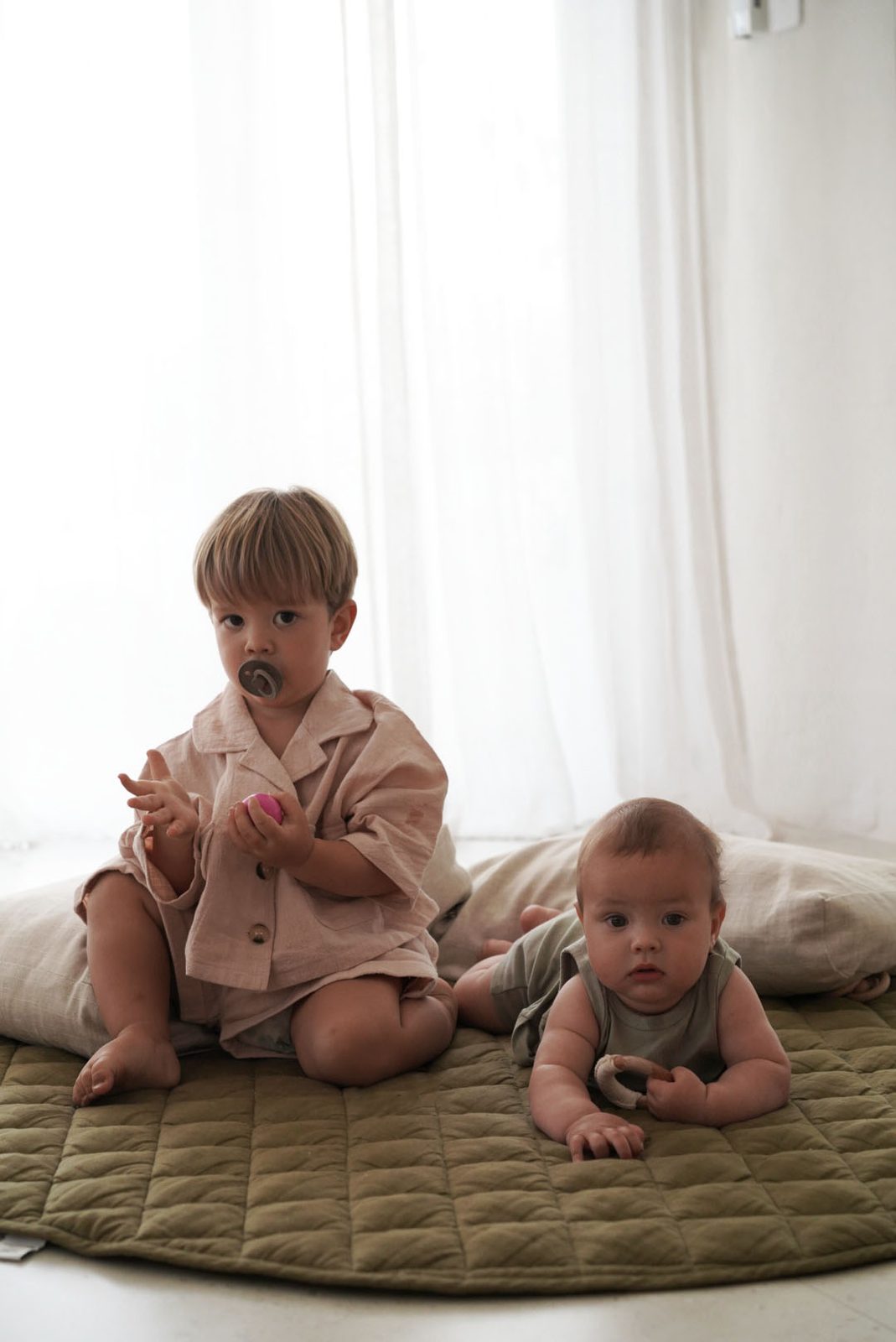 Toddler and a crawling baby sitting together on a green quilted play mat