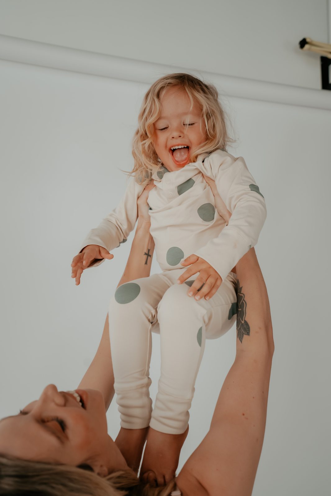 Mother lifting a laughing toddler in a polka dot outfit overhead