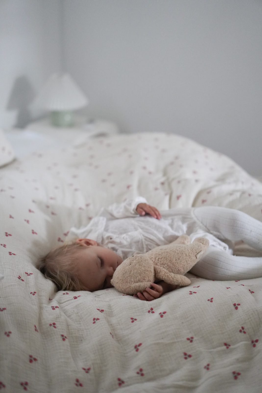 Toddler sleeping peacefully on a floral quilt, cuddling a soft bunny toy