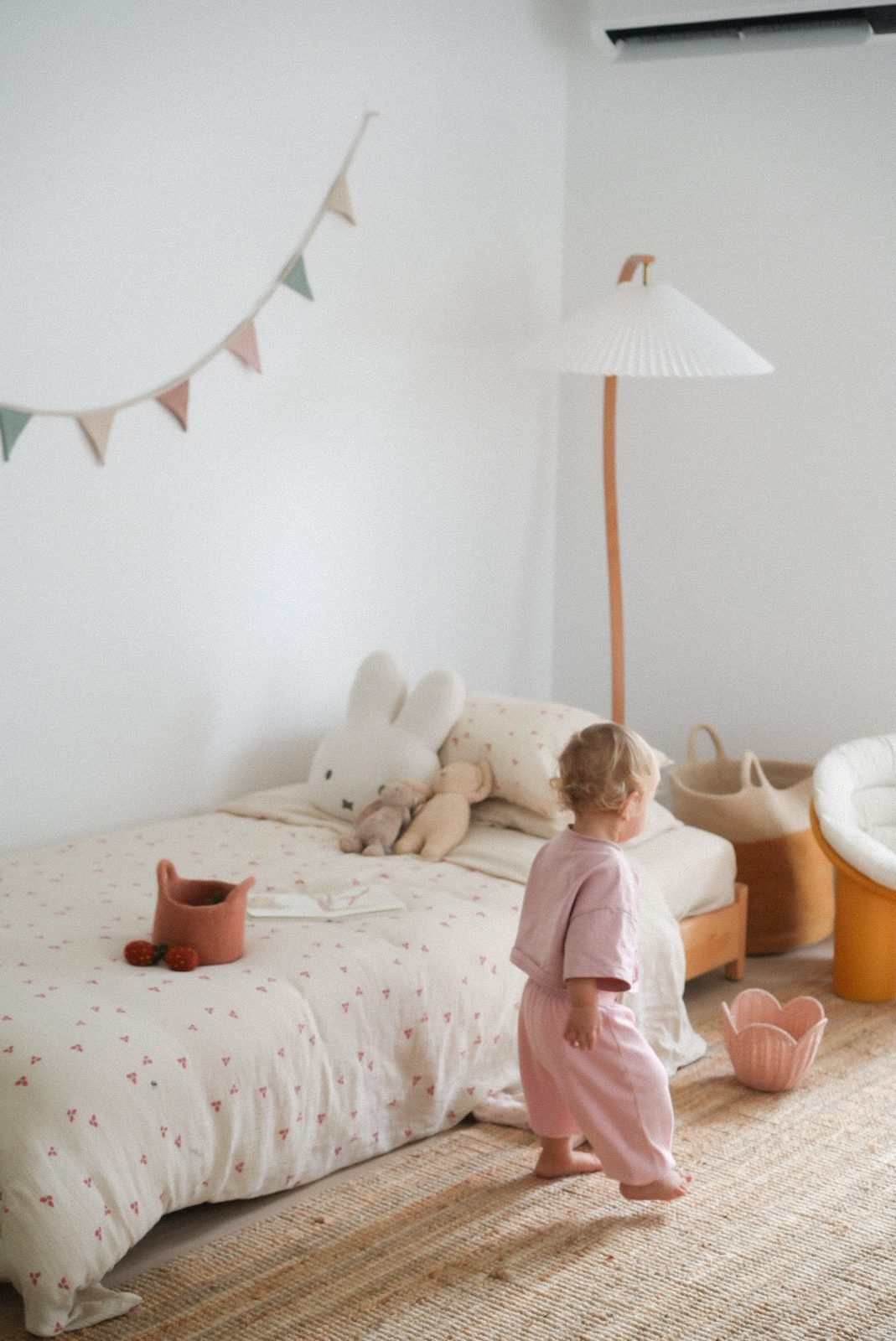 Toddler in pink knit outfit walking through a styled bedroom with toys