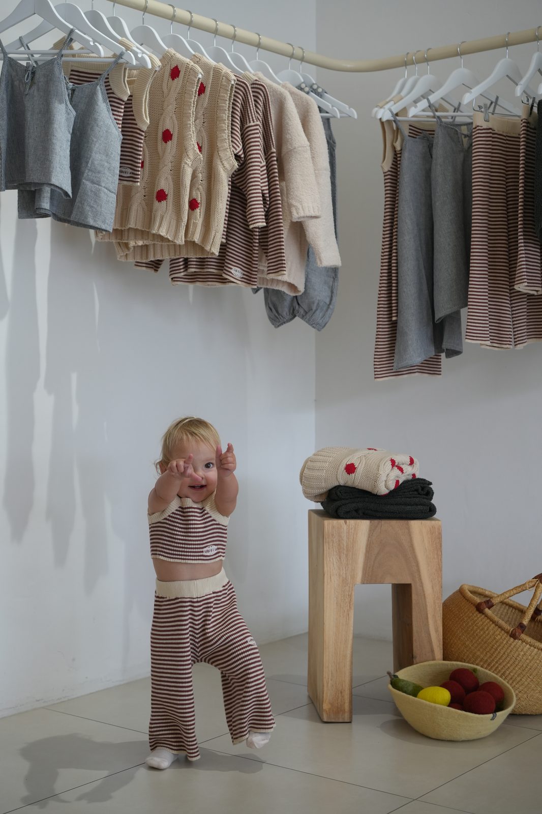 Toddler girl in striped knit playsuit playing peekaboo in a children's clothing boutique