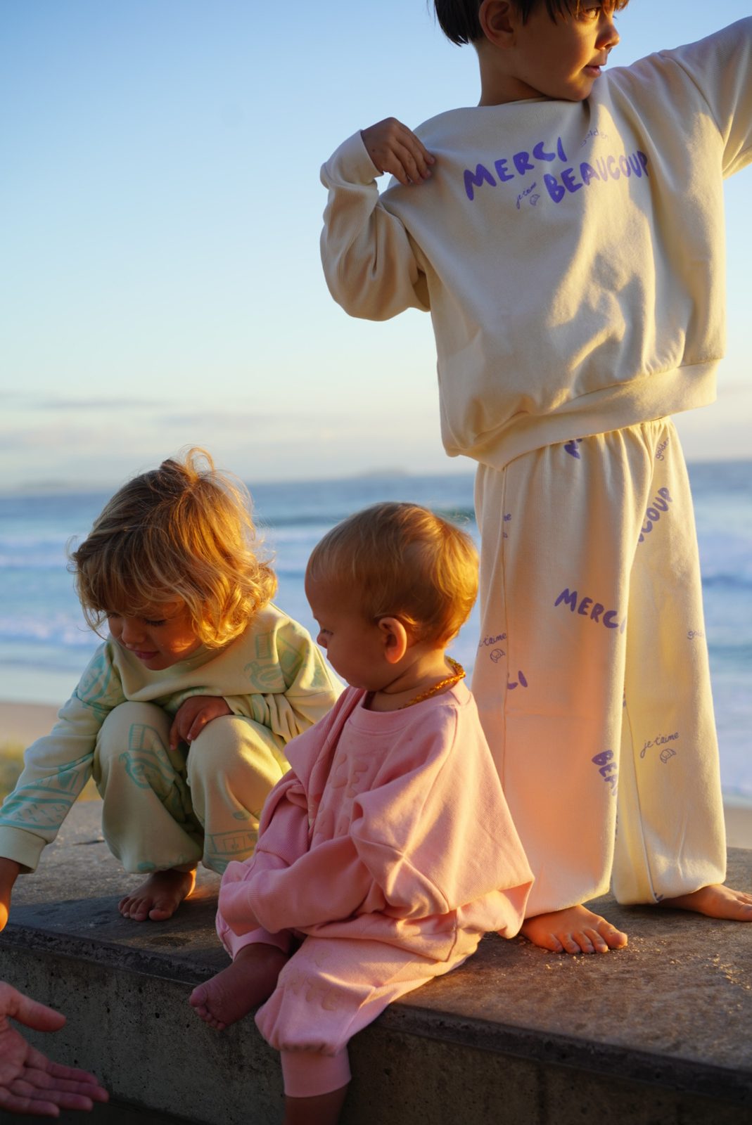 Three children in coordinated Golden brand sweatsuits at the beach