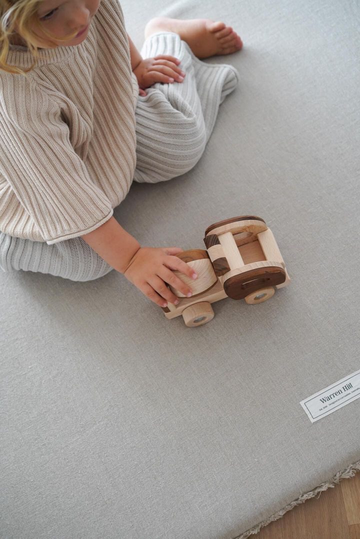 Overhead shot of a toddler reaching for a handcrafted wooden toy truck on a linen mat