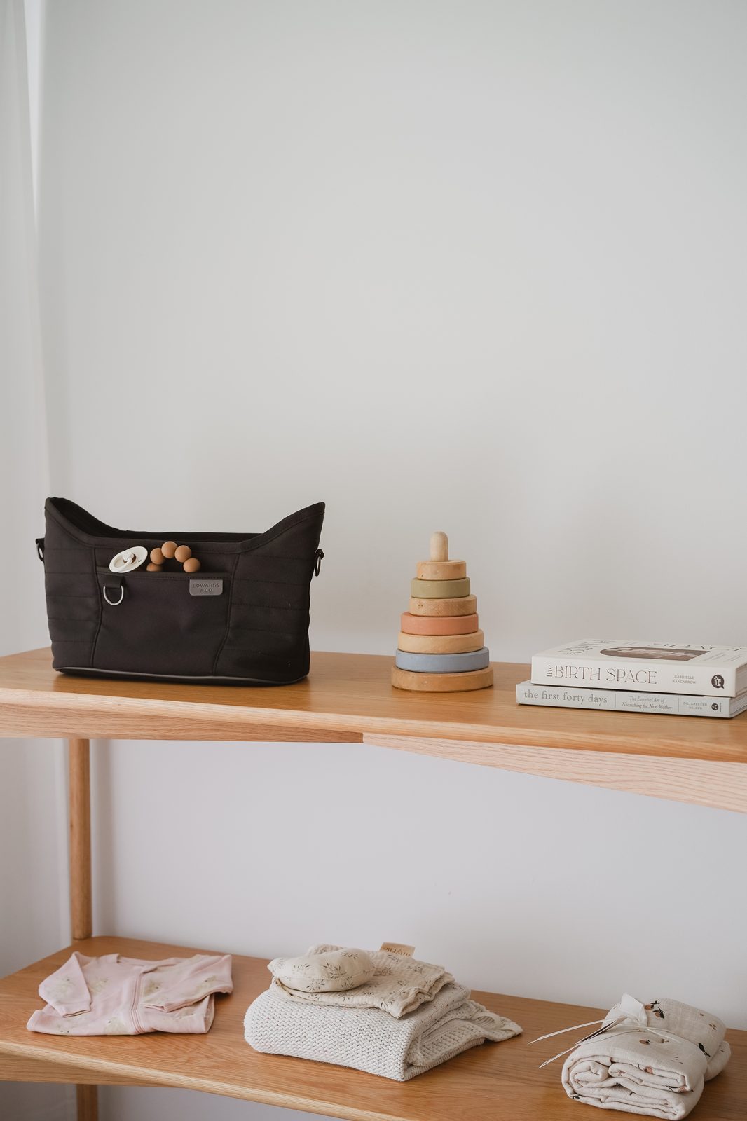 Flat lay of baby gear including a nappy bag, wooden stacking toy, books, and knitwear