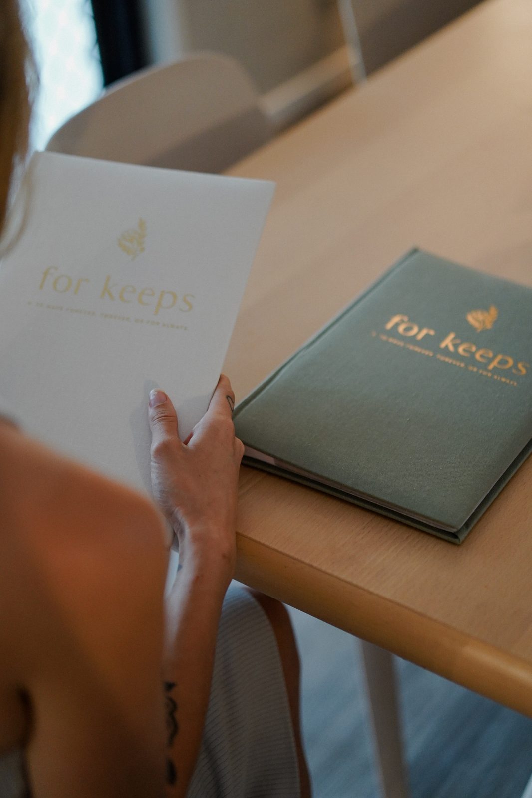 Hand holding a 'For Keeps' keepsake journal beside its matching linen cover edition