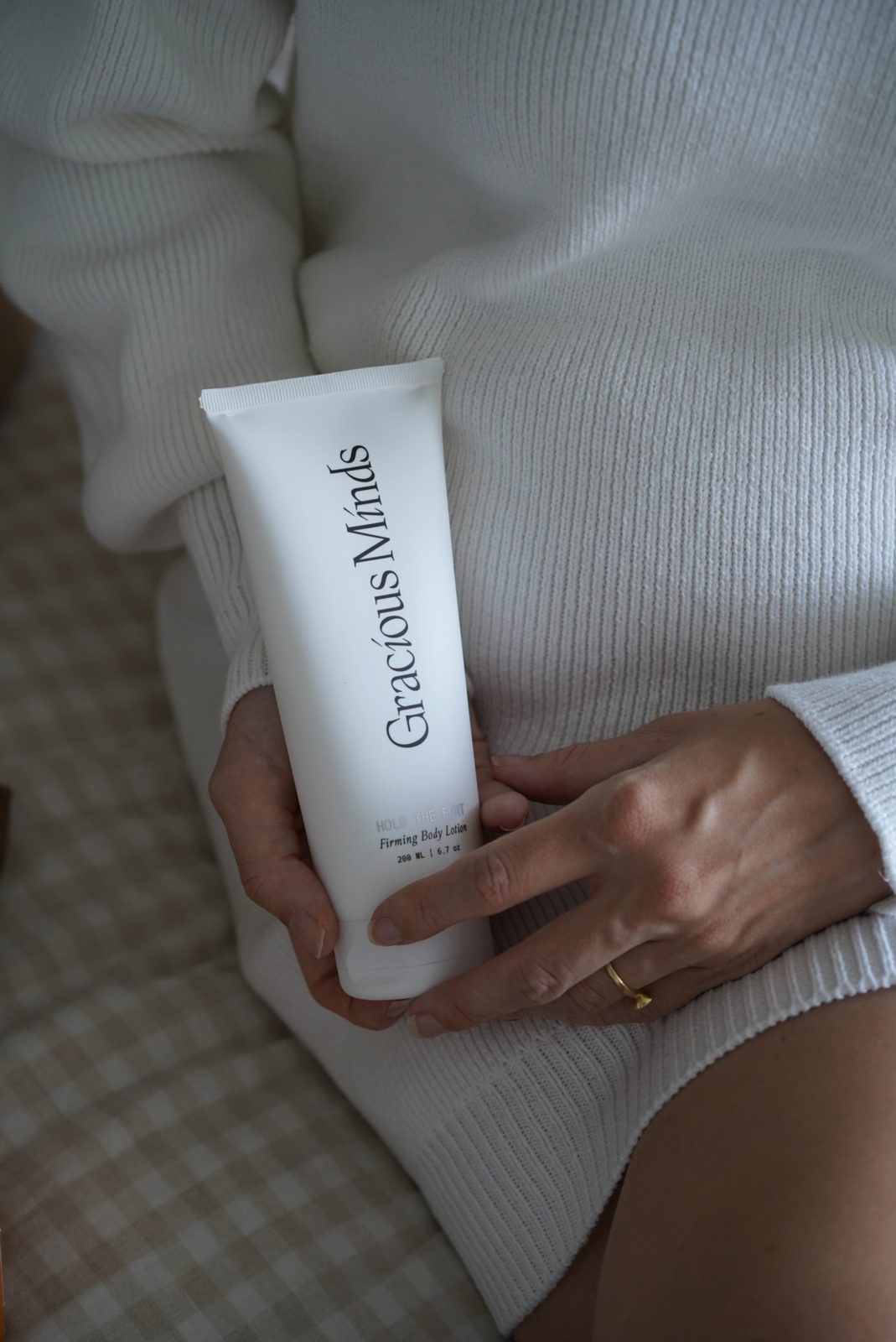 Hand holding a tube of Gracious Minds firming body lotion