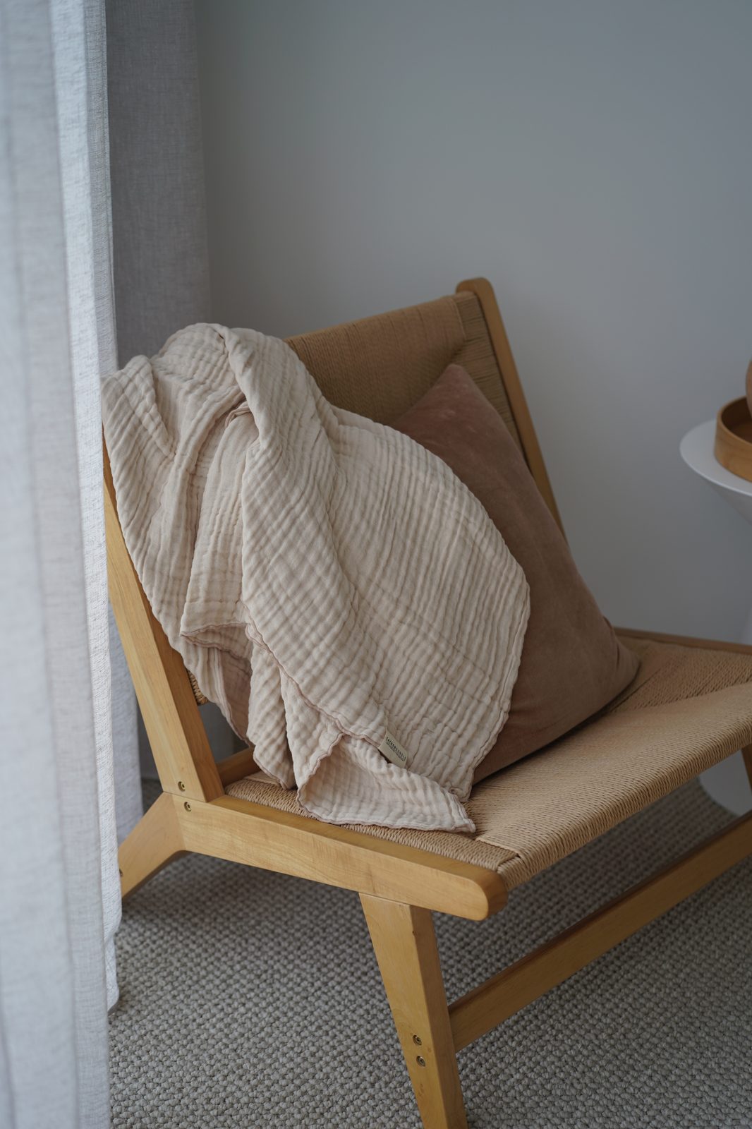 Muslin baby wrap and velvet cushion styled on a woven lounge chair