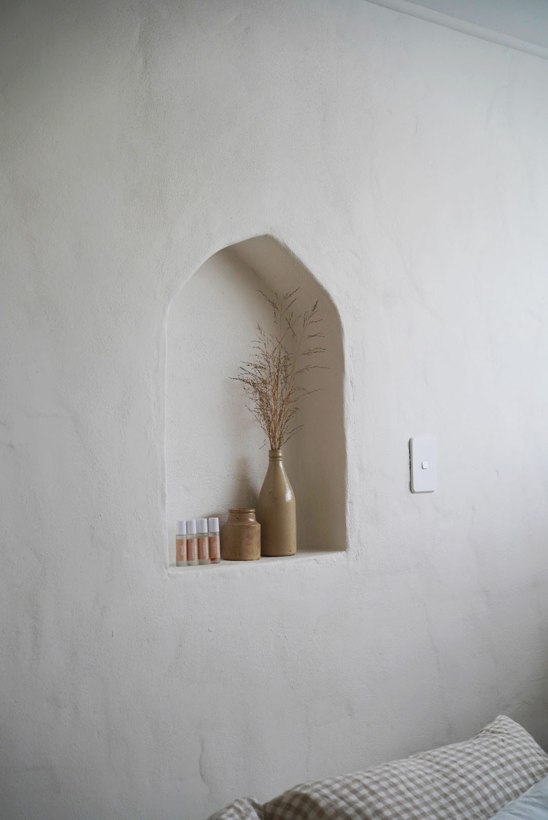Skincare rollerball bottles and a ceramic vase styled in a plastered wall niche